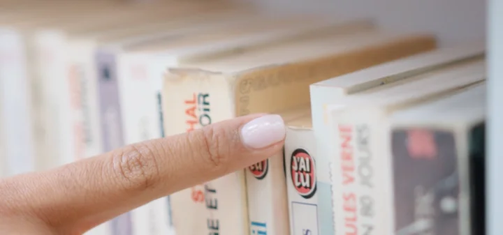 Finger pointing at a row of paperback books on a shelf